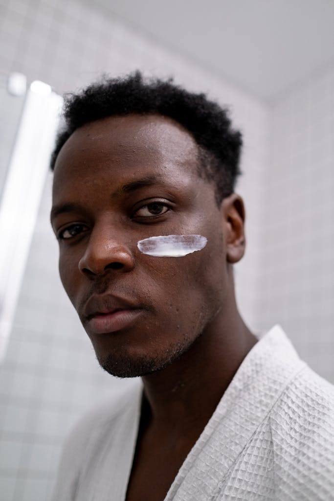 Man with cream on face in bathroom, promoting skincare routine and self-care.